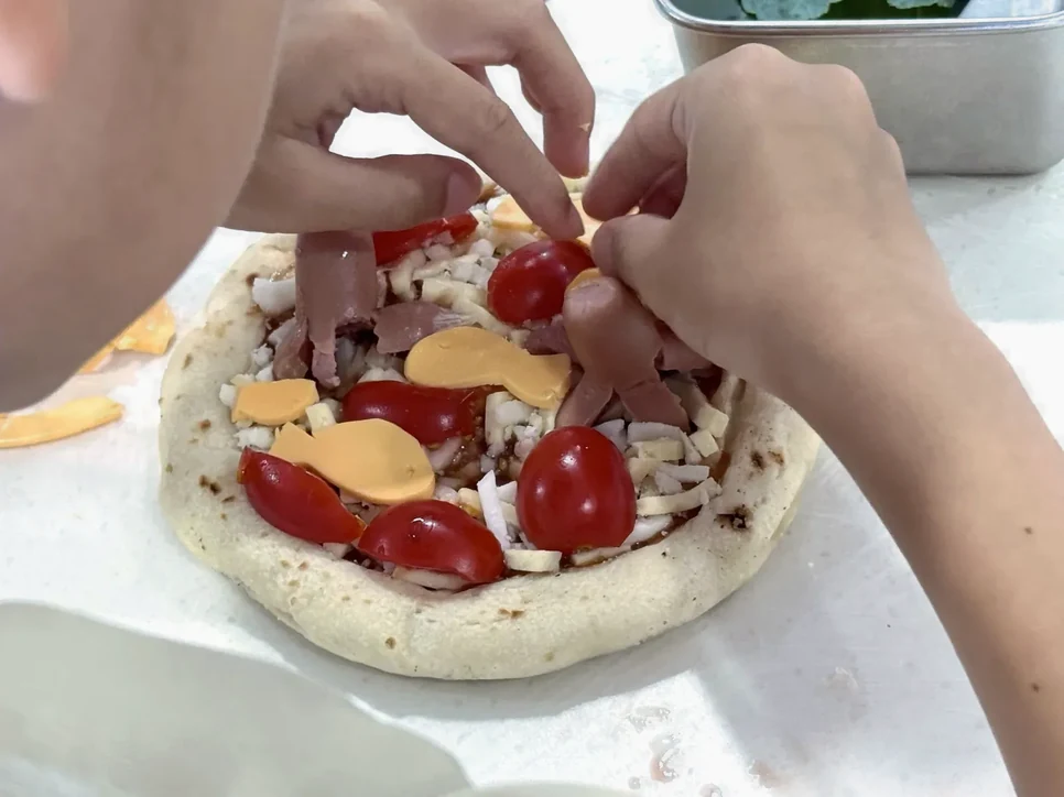 순창 고추장 요리 체험 안내: 소스를 바른 피자에 토마토와 치즈를 올리는 손